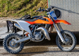 orange dirt bike parked next to a truck and ready for competition