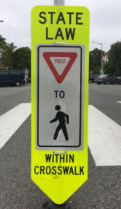 tall yellow pedestrian paddle sign at a crosswalk