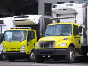 a big refrigerator truck parked with a similar smaller vehicle