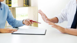 a man being handed a pen to sign a document and raising his hands in refusal